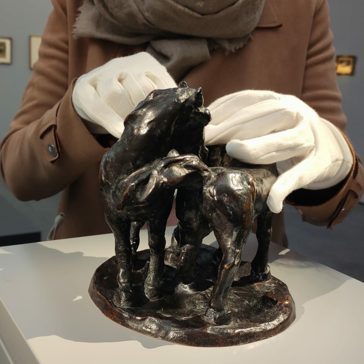 Abgebildet ist die Bronzeplastik "Zwei Pferde" von Franz Marc im Ausstellungsraum. Sie steht auf einem hellgrauen Sockel. Eine Person ertastet die Plastik mit weißen Baumwollhandschuhen. 